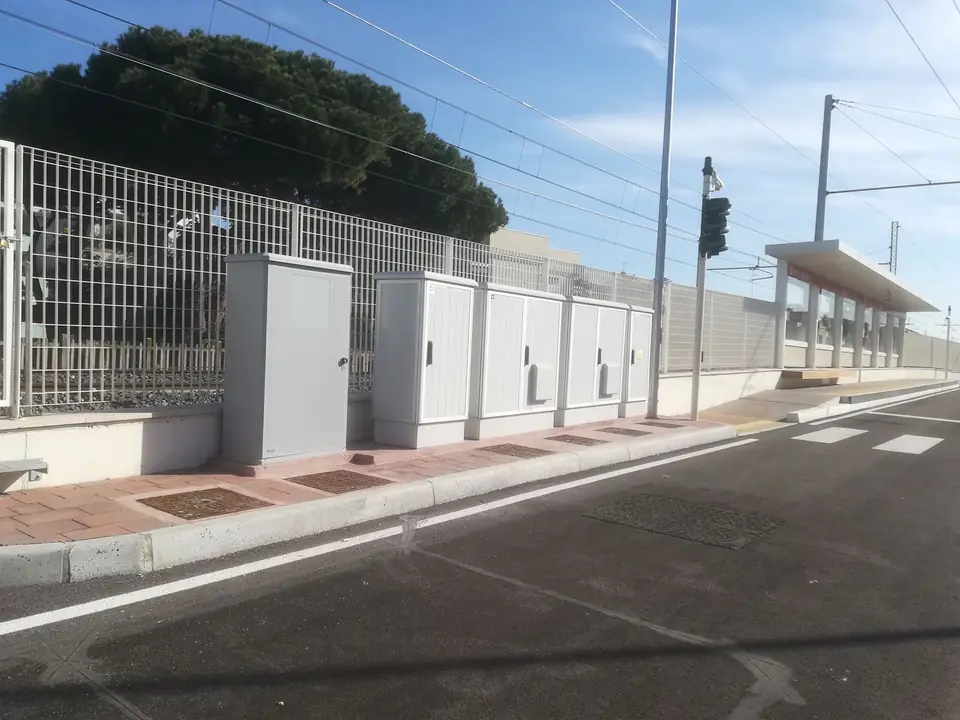 Outdoor enclosures in a row next to the busway, stop canopy and overhead line behind